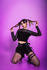 Girl posing on her knees in grunge style with yakrim makeup holding ponytails with her hands on a purple background