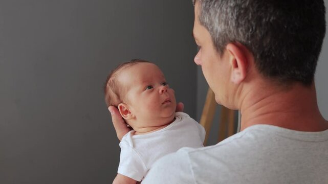 Unrecognizable man wearing white casual T-shirt with infant baby in hands in home interior loving dad rocking baby to sleep looking at child hugging his cute daughter or son