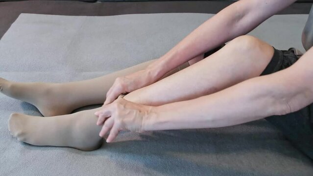 A 57-year-old woman puts on compression stockings at home.
Concept for the prevention and treatment of varicose veins, lipedema, spider veins on the legs, thrombosis of the legs during a long flight.