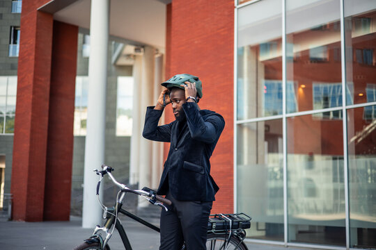 black african american businessman dons helmet to commute sustainably on electric bicycle - Powered by Adobe