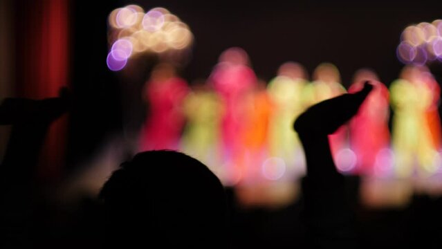 children's concert on stage out of focus, in the auditorium the audience clap their hands and dance, children's reporting concert for parents