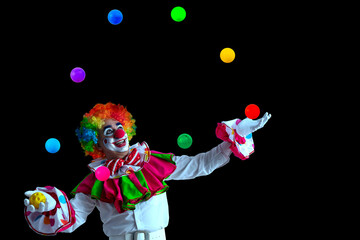 Funny juggler clown juggling balls in the circus, man entertainer as Joker in a suit and wig, with clown whiteface makeup. Trickster, jester, pantomime, mime, and a professional actor at events.