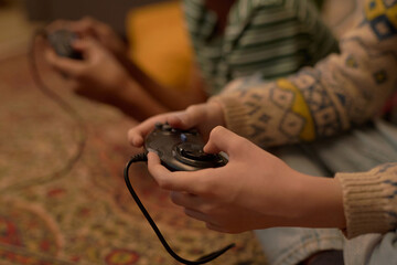 Close-up of boys hands holding a retro video game controllers, sitting on the carpeted floor and deeply engaged in vintage gameplay