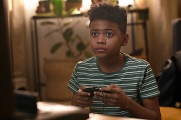 African American teenage boy with short curly hair playing retro video game, focused on the screen while sitting on the floor in a cozy old-fashioned living room