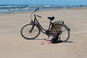 Fototapeta premium Ein schwarzes Fahrrad steht am Strand, Schuhe und ein Rucksack stehen davor 