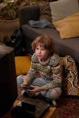 Vertical shot of male Caucasian teenager sitting cross-legged on carpeted floor with retro...