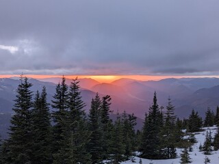 Cloudy sunset over snowy mountain pine forest