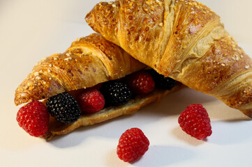 Homemade fresh croissant. Fragrant pastries on a white background with raspberries and other berries. Ecological concept. View from above