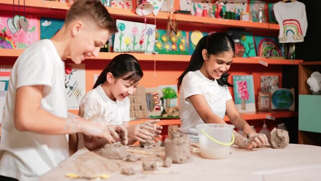 Caucasian high school girl modeling cup of clay while looking smart boy in art class at workshop. Multicultural student playing or making cup of clay art in creative activity. Education. Edification