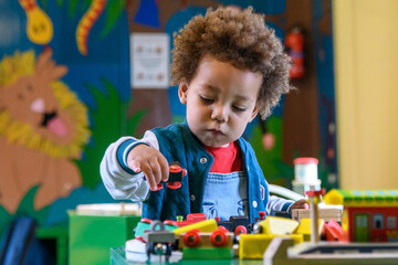 Toddler playing with a train set at nursery, kinder garden. Multi ethnic boy at playtime. ...
