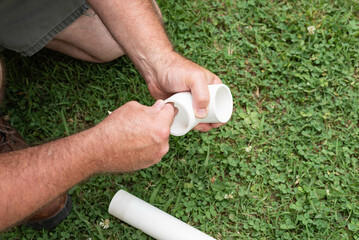 Male hands sanding a pipe to receive primer and glue to fit together a PVC line.