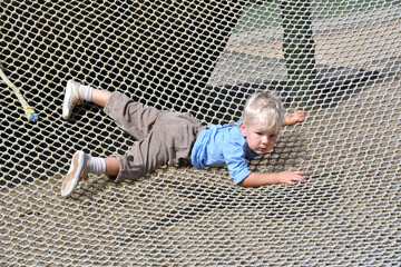 Happy little boy climbing on the rope net in adventure activity park