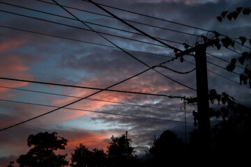 Color sky after sunset with silhouette of electric villages wires and dark trees