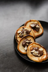 Plate of pancakes dripping with Nutella and almond crumbs with dark gray background.. Copy space for text. Mockup for menu, Pancake day