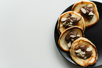 Plate of pancakes dripping with Nutella and almond crumbs with dark gray background.. Copy space for text. Mockup for menu, Pancake day