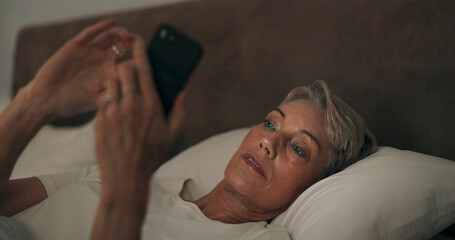 Reading, bed and mature woman with phone for online blog on insomnia, sleep apnea or relaxing. Communication, night and senior female person networking with email on smartphone in bedroom at home.