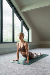 Peaceful young caucasian woman yoga instructor is practicing vinyasa flow, upward facing dog yoga ashtanga asana pose indoors. Wellness, lifestyle, copy space.