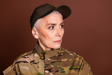 Photo of attractive confident elderly lady dressed camo uniform looking empty space isolated brown color background