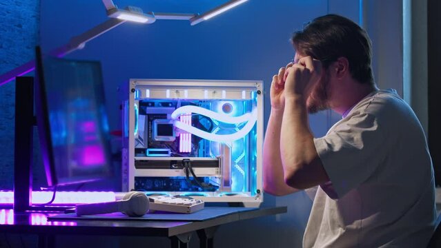 Young man puts on his glasses and continues working at the computer. With the glasses, he can see much better and his eyes don't get tired. Medium shot. Slow motion.