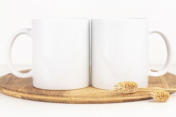Mockup of two coffee white mugs on wooden tray with dried flowers, neutral color. Blank 10 oz cups mock up in Boho style.