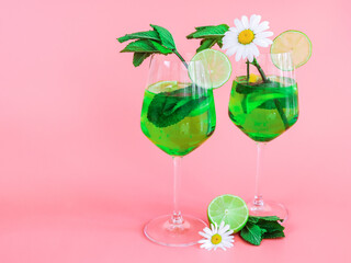 Two glasses of mojito alcoholic drink with green lime,mint and daisies on the right on a pink .