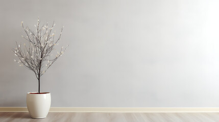Bare branches of a tree in a pot stand against a plain, light-colored wall.