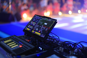 Close-up of advanced audio-visual control equipment at a vibrant event, featuring screens and...