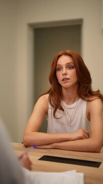 Vertical portrait of focused millennial female applicant in casual clothes holding interview conversation with professional hr manager in modern office, discussing experience or job offer at meeting.