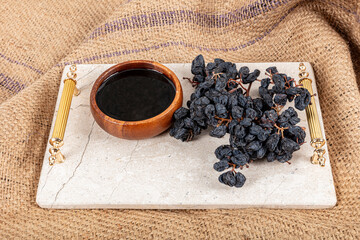 Grape molasses in wooden bowl, dried black grapes in wooden spoon and on burlap background, healthy...