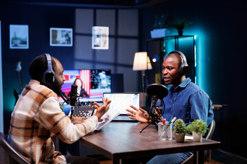 Two black men having a serious conversation and recording it for their online listeners. African American male content creators sitting at home and using audio equipment for making a live talk show.