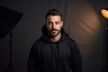 A man in a black hoodie is standing in front of a light