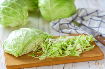 Whole and sliced fresh green cabbage on a white wooden table.