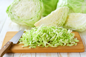 Whole and shredded cabbage on light wooden table.