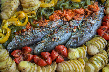 Delicious baked rainbow trout fish with spices and colorful vegetables grilled cooked with herbs, red tomatoes, carrot, sliced potatoes and green, yellow paprika. Close up. Top view