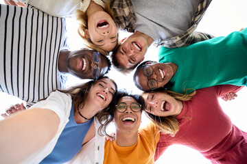 Selfie from below of large group of diverse friends posing hugging in circle looking excited at...