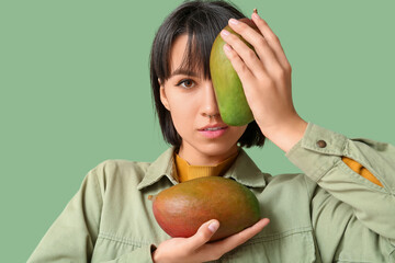 Beautiful young woman with ripe mangoes on green background