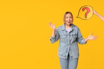 Surprised adult woman and female hand holding speech bubble with question mark on yellow background
