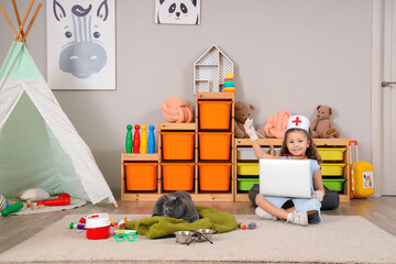 Cute little girl with British cat, laptop and first aid kit at home