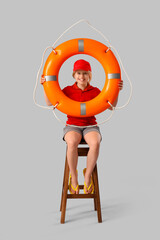 Happy little girl lifeguard with ring buoy sitting on chair against grey background