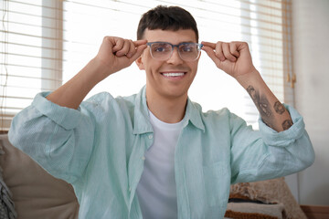 Handsome happy young man in new stylish eyeglasses at home