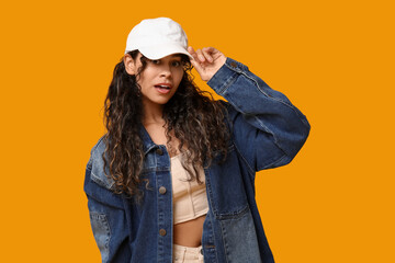 Young African-American woman in baseball cap and stylish clothes on yellow background