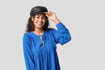 Stylish African-American woman wearing dress and hat on light background
