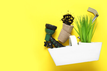 White crate with gardening supplies and plant on yellow background