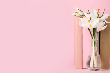 Glass vase with beautiful white crocus flowers and books on pink background