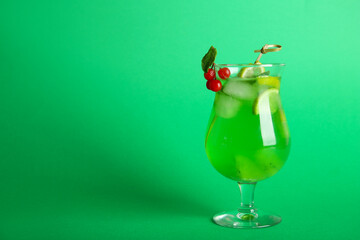 Glass of tasty cocktail with lime and cranberry on green background