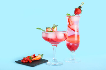 Glasses of tasty cocktail with strawberry and cranberry on blue background