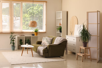 Interior of beautiful living room with folding screen, comfortable sofa, chest of drawers and coffee table
