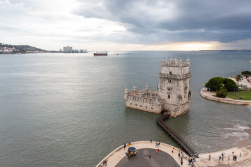 Belem Tower overlooking aerial view. Fortress monument in Lisbon on Tagus River. 16th-century fortification Torre de Belem in city under cloudy sky. Evening time