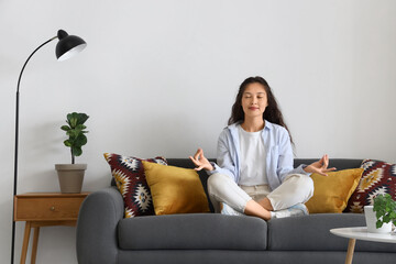 Young Asian woman meditating on black sofa at home