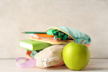 Turquoise backpack with stationery and green apple on table against white grunge wall